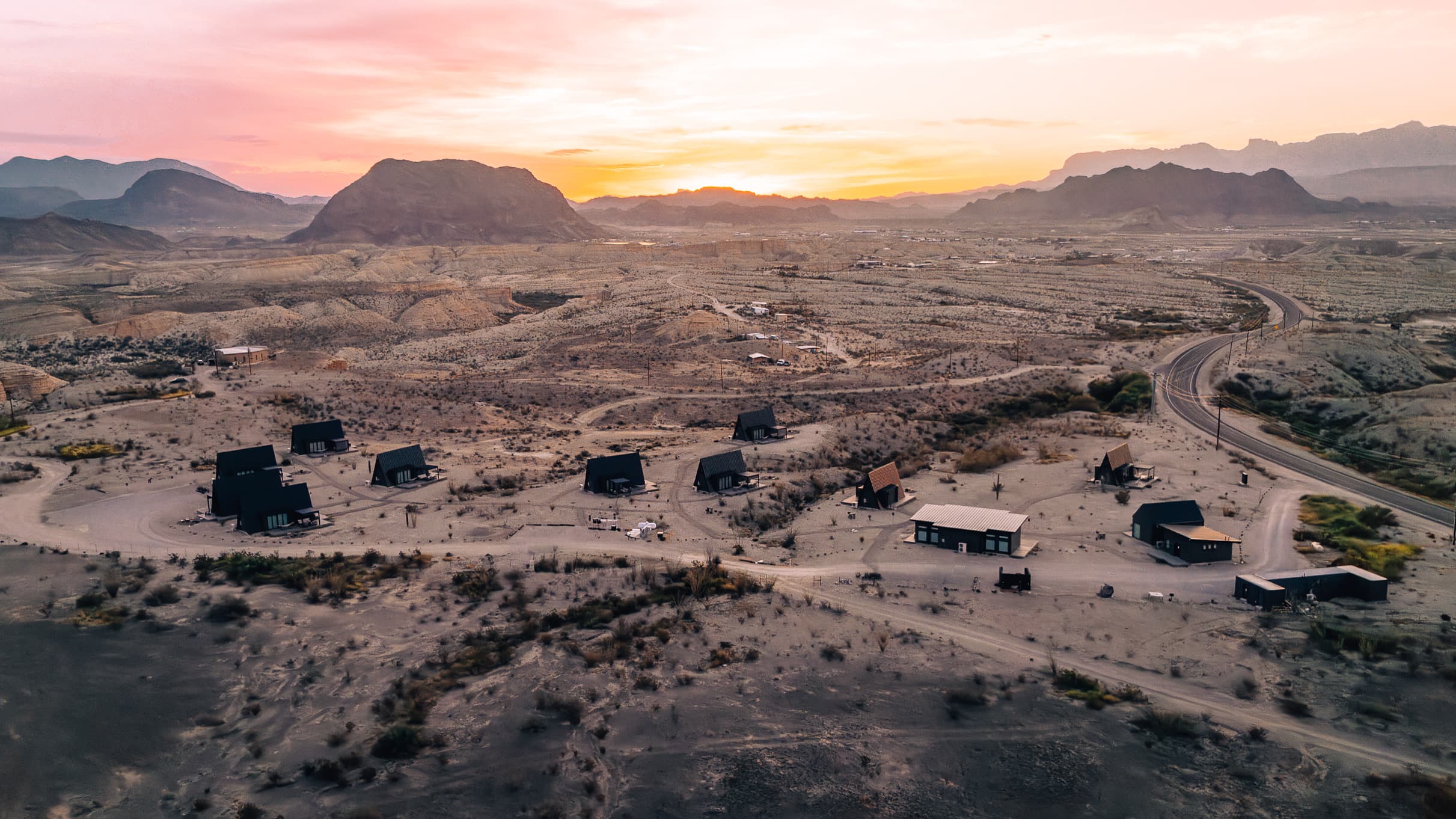 Aerial view of the Stardust Big Bend property at sunset, with the cabins spread across the desert and the mountains beyond